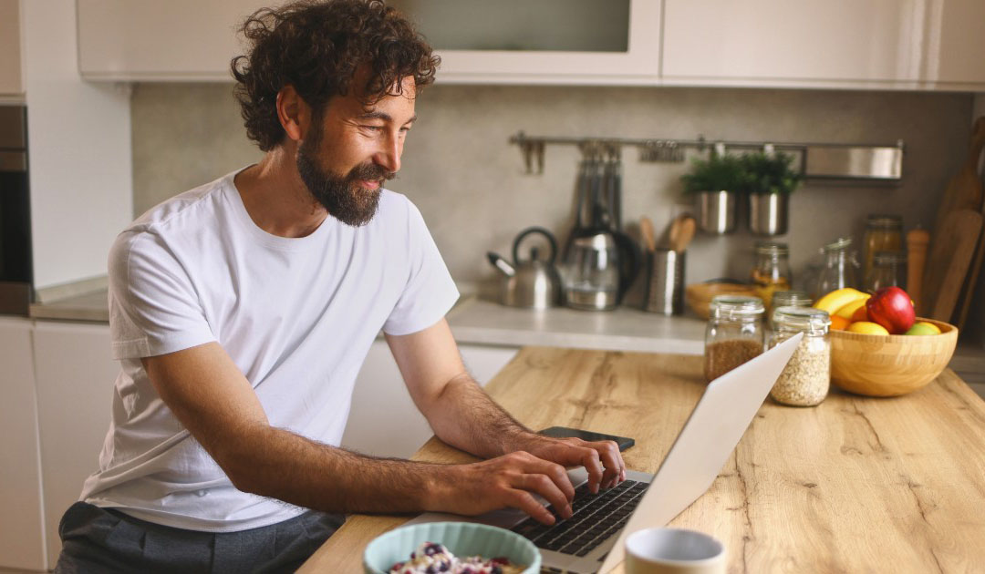 Man working on a laptop on a kitchen counter - mindful Mondays tips